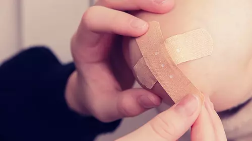 En hand plåstrar om ett knä efter ett olycksfall